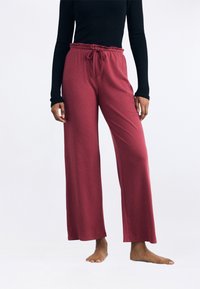 Bordeaux kleurige wijde broek met een ribbeltextuur, een elastische tailleband en een trekkoordsluiting. Draagt met een zwart langgevormd top en op blote voeten.