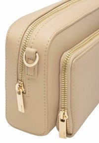 Beżowa skórzana torba z dwoma komorami na zamek, z złotymi zamkami i elementami metalowymi, prostokątny kształt o gładkiej fakturze.