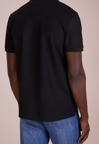 černé polo tričko s krátkým rukávem vyrobené z texturované tkaniny, s klasickým límečkem a bočními rozparky, v kombinaci s modrými denimovými džíny.