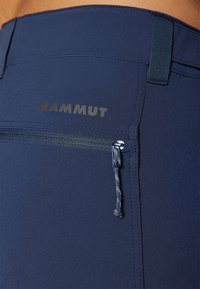 Tamsiai mėlynos sportinės kelnės su užtrauktuku kišene, elastingu juosmeniu ir kontrastingos spalvos "MAMMUT" logotipu. Lygus, tamprus audinys.