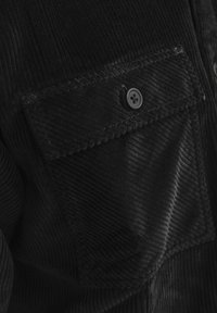 Black corduroy shirt featuring a textured surface, buttoned chest pocket, and neatly stitched edges, highlighting durable material.