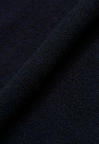 Dunkelblauer Stoff mit einer weichen, strukturierten Oberfläche, einem dicht gewebten Muster und einem leichten Glanz, der an einer Kante aufgerollt ist.