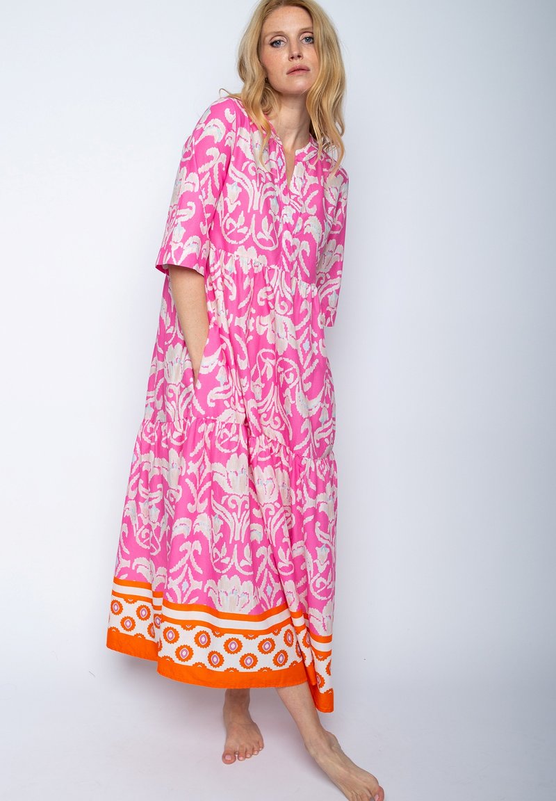 Rosa gemustertes Kleid mit kurzen Ärmeln, gestufter Design und Taschen. Verfügt über einen orangenen und weißen Akzent am Saum.