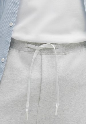 Hellgraue Jogginghose mit weichem Material, ausgestattet mit einem weißen Kordelzug und einem gerippten Taillenbund. Oberhalb ein blau gestreiftes Hemd mit Knöpfen.