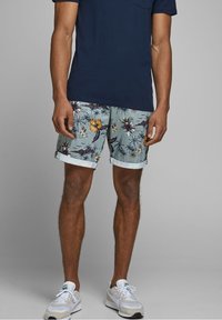 Šortky s květinovým potiskem v světle modré barvě s ohrnutými nohavicemi. Materiál vypadá lehký. Doplněné tmavě modrým tričkem a sportovními teniskami.