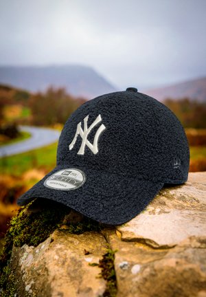 New Era baseball cap in dark navy fleece, featuring a contrasting white NY logo, rounded shape, and adjustable strap. Tag visible on brim.