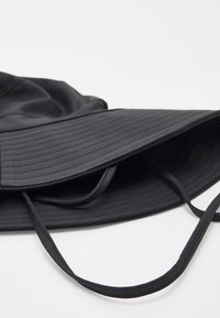Black bucket hat made of smooth fabric, featuring a wide, ridged brim and adjustable straps. The design is simple and folding.