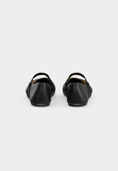Paire de ballerines en cuir noir avec des sangles élastiques vues de dos sur un fond clair uni.