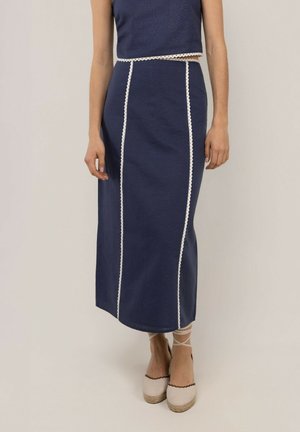 Mujer que lleva una falda midi azul marino con rayas verticales de encaje blanco y zapatos de esparto crema con lazos en el tobillo.