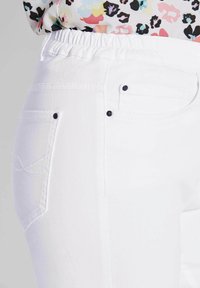 Witte broek met een elastische tailleband, zij- en achterzakken met zwarte hardware-accenten en een gladde, lichte stoftextuur.