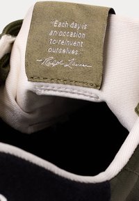 Närbild av en skotunga med en grön tygetikett som säger: "Varje dag är ett tillfälle att återskapa oss själva." signerad av Ralph Lauren.