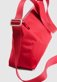 Κόκκινη τσάντα από νάιλον με ορθογώνιο σχήμα, διαθέτει κλείσιμο με φερμουάρ και ιμάντα ώμου από υφασμάτινο πλέγμα, με λεία υφή και μινιμαλιστικό σχεδιασμό.