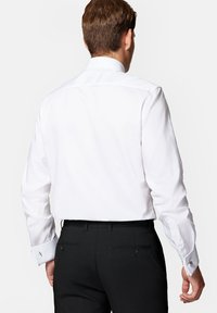 Biała koszula z długim rękawem, z ostrym kołnierzykiem i mankietami na spinki, w zestawieniu z czarnymi spodniami. Gładki materiał o dopasowanym kroju i subtelnym przeszyciu.