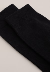 Svarta bomullsbenvärmare med ribbat mönster och breda toppar, placerade parallellt med varandra på en ljus bakgrund.