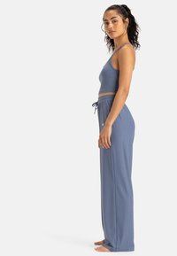 Top court côtelé bleu clair et pantalon ample avec taille à cordon. Le tissu semble doux ; branding minimal sur le pantalon près de la taille.