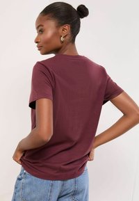 Burgundia lühikeste varrukatega T-särk klassikalise ümarakaelusega, pehme kangas, lõdvestunud lõige ja tagaõmbluse detail, sobitatud siniste denimidest teksadega.