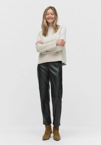 Beige gebreide trui met lange mouwen, gecombineerd met zwarte neplederen broek en bruine suède enkellaarsjes. Neutrale kleuren en minimalistisch ontwerp.