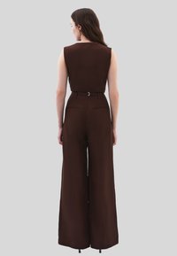 Hnědý overal bez rukávů s pevně střiženým pasem a širokými nohavicemi, který se vyznačuje hladkou texturou a minimalistickým designem.