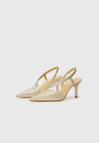 Kuldne sädelevaid slingback-kandaga kontsasid, millel on terav nina, õhuke konts ja ristatised rihmad. Sile sisemus ja tekstureeritud pealis.