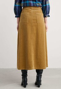 Br�ūna korduroja garā svārku ar divām aizmugures kabatām un taisnu siluetu, apvienota ar melniem ceļgala augstiem zābakiem. Tekstūrēta auduma rievotā rakstā.