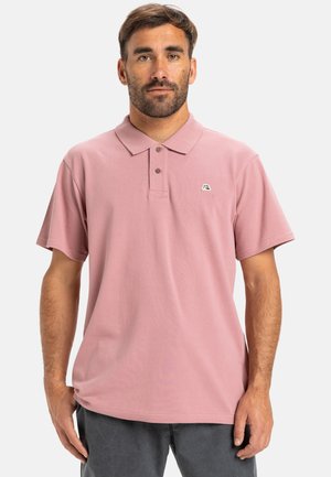 Polo de color rosa claro con mangas cortas, un cuello, tres botones y un pequeño detalle de logo en el pecho. Material de algodón suave.