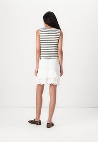 Haut sans manches noir et blanc à rayures avec un col rond, associé à une jupe en dentelle blanche à volants. Des ballerines à imprimé léopard viennent compléter le look.