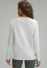 Jasnoszara koszula z długim rękawem i okrągłym dekoltem, o teksturowanej fakturze i centralnym szwie. Połączona z zielonymi szortami, prezentującymi swobodny krój.