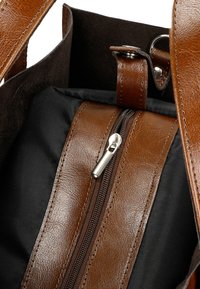 Bruine lederen handtas met een zwarte stoffen binnenkant, voorzien van een zilveren ritssluiting en stevige bruin leren handvatten. Glad van textuur met een subtiele glans.