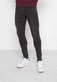 Schwarze Slim-Fit-Denimjeans mit leichtem Stretch, ausgestattet mit fünf Taschen und dezenten Nähten, kombiniert mit weißen Turnschuhen.
