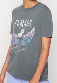 Tummanharmaa puuvillainen t-paita lyhyillä hihoilla, jossa on graafinen kuvasto siivistä, päivänkakkaroista ja teksteistä valkoisena sekä pastelliväreissä.