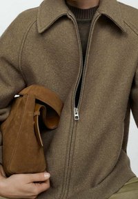 Brązowa kurtka z mieszanki wełny z zamkiem błyskawicznym i kołnierzem; w połączeniu z małą brązową torebką ze zamszu, eksponującą gładkie faktury i ciepłe odcienie.