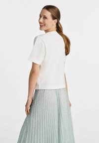 Biała krótka bluzka z krótkim rękawem połączona z plisowaną spódnicą w miętowym kolorze, zdobioną delikatnym kwiatowym wzorem, na jednolitym tle.