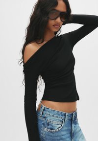 Zwarte lange mouwen top met een asymmetrische halslijn, gecombineerd met lichtblauwe denim jeans met een klassieke pasvorm en studs.