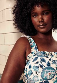 Virágmintás ruha kék, zöld és fekete mintákkal fehér háttéren. Ráncolt pántokkal és fitted bodiccel rendelkezik.