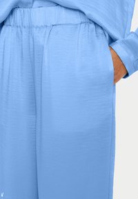 Light blue, loose-fitting pants with an elastic waistband and side pockets. The fabric has a smooth texture and subtle sheen.