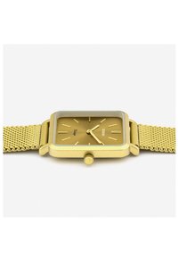 Montre carrée dorée avec un bracelet en maille. Présente un cadran minimaliste, des index en or, et une petite couronne. Fini lisse et mat.