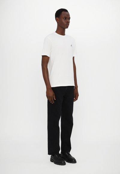 White cotton t-shirt with a small logo on the chest, paired with black straight-leg jeans and black lace-up shoes. Simple design.