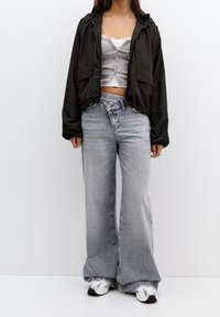 Giacca nera corta con cappuccio, top grigio aderente e jeans larghi grigio chiaro. Scarpe in argento, sneakers. Insieme semplice e casual.