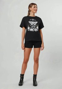 T-shirt preta com estampa gráfica branca com uma borboleta, flores e elementos celestiais, combinada com calções pretos e botas até ao tornozelo.