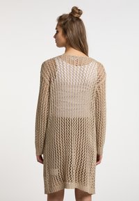 Cardigan in maglia beige con un'apertura a trama larga. Presenta maniche lunghe e un orlo arrotondato, evidenziando un design trasparente.