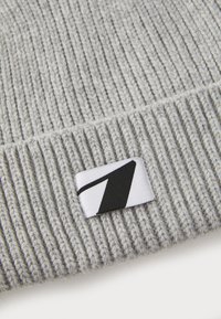 Bonnet en tricot gris, avec une texture côtelée. Comprend un patch logo noir et blanc pour le branding. Construction en fil épais.