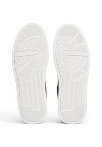 Pair of shoes with white textured soles featuring circular, zigzag, and linear patterns, branded with "Tommy Hilfiger" on the bottom.