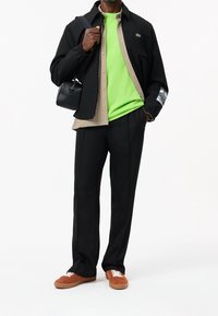 Czarna kurtka z koszulą w kratę pod spodem, żywy zielony top, czarne spodnie i brązowe sneakersy z białymi sznurowadłami; mała czarna torba.