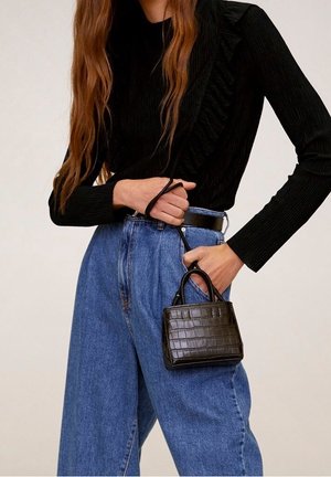 Sac à main en cuir de crocodile noir avec deux poignées courtes, forme rectangulaire, associé à un t-shirt noir à manches longues à côtes et un jean bleu taille haute.