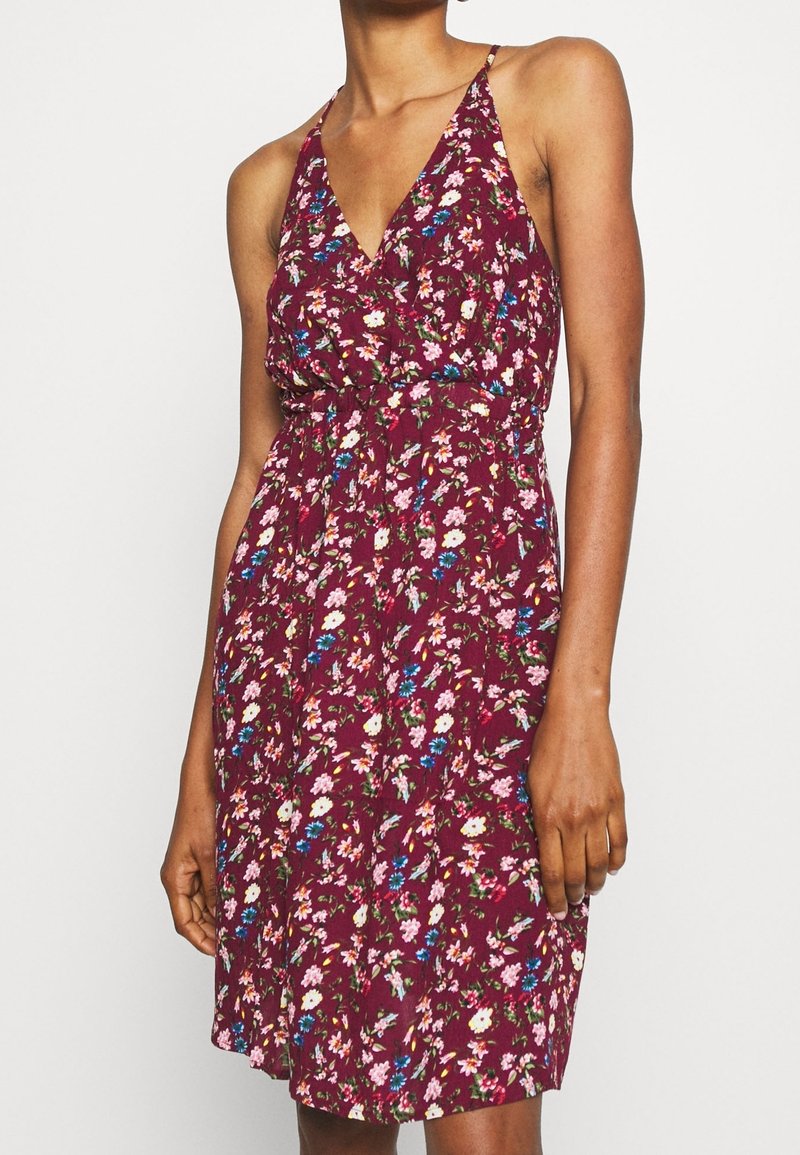 Květinové šaty v burgundské barvě, s výstřihem do V, ramínky na špagetách a nařaseným pasem. Design obsahuje vícebarevné květiny na jemném materiálu.