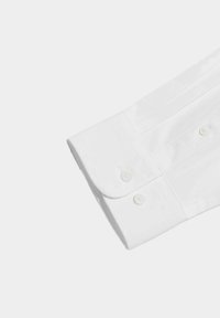 Puño de camisa blanca de algodón que presenta un borde redondeado, dos botones y sutiles pliegues para textura. Acabado suave y nítido.