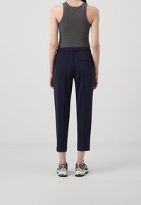 Pantalon fuselé bleu marine avec une ceinture élastique, une poche arrière et des revers roulés, assorti à un débardeur gris et des chaussures de sport.