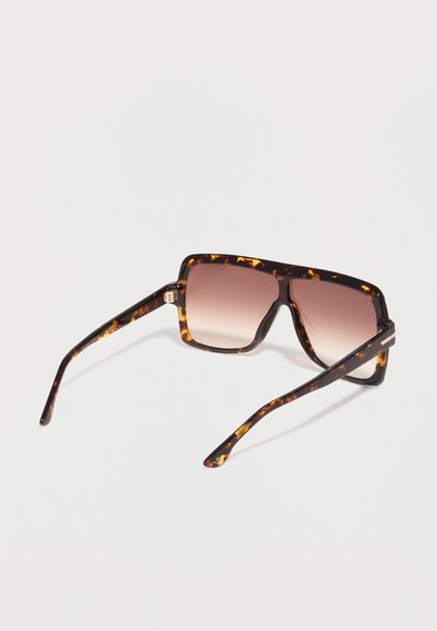 Ορθογώνια γυαλιά ηλίου με σκελετούς από χελώνα και φακούς καφέ με βαθμιαία απόχρωση, τοποθετημένα πάνω σε λευκή επιφάνεια.