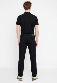 Polo nero a maniche corte, abbinato a jeans neri slim-fit. Le scarpe con suola in gomma presentano accenti verdi e beige.