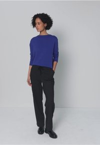 Blue long-sleeve sweater with a crew neckline paired with black drawstring trousers. The outfit features a relaxed fit and smooth texture.